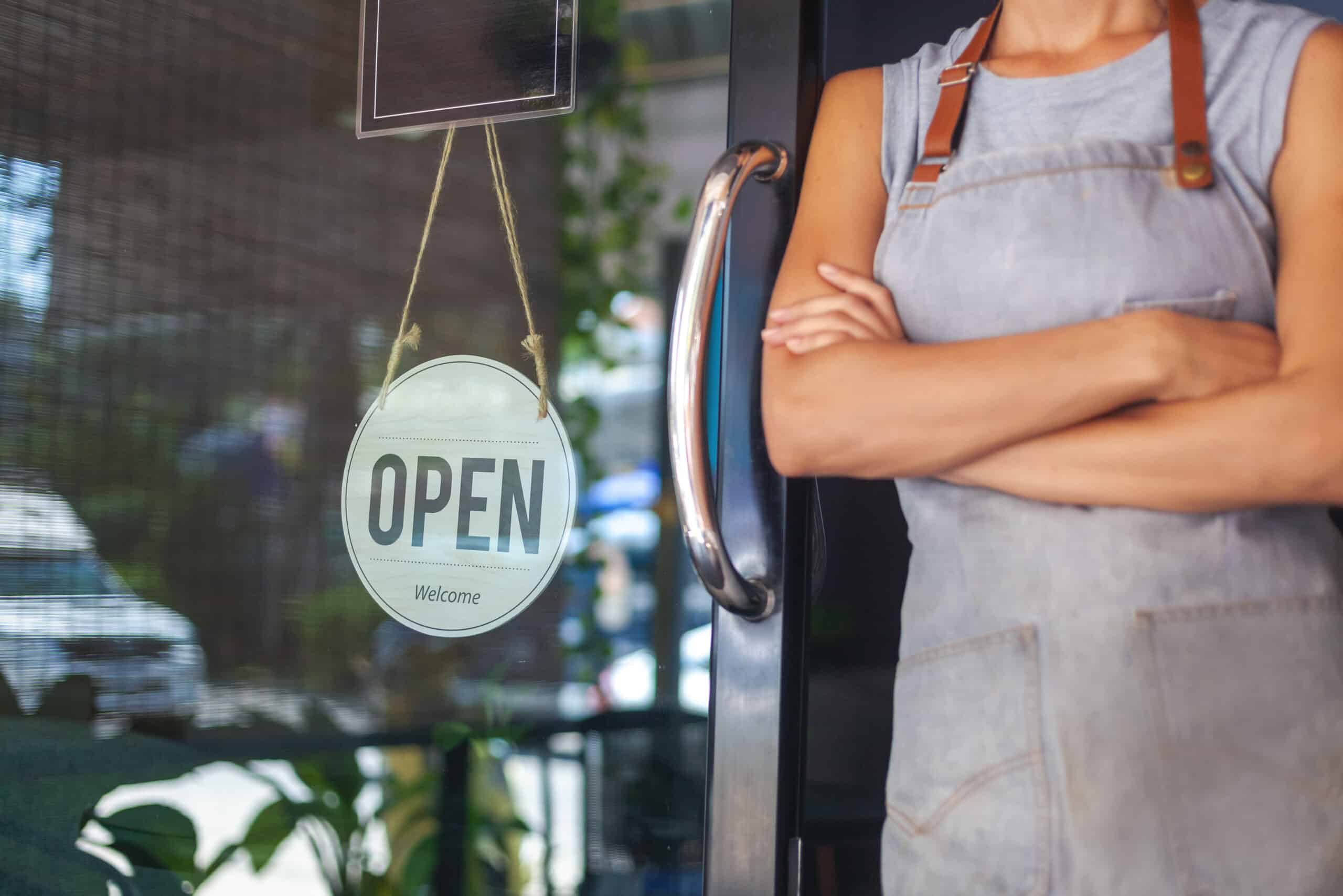 The woman is a waitress in an apron, the owner of the cafe stands at the door with a sign Open waiting for customers. Small business concept, cafes and restaurants